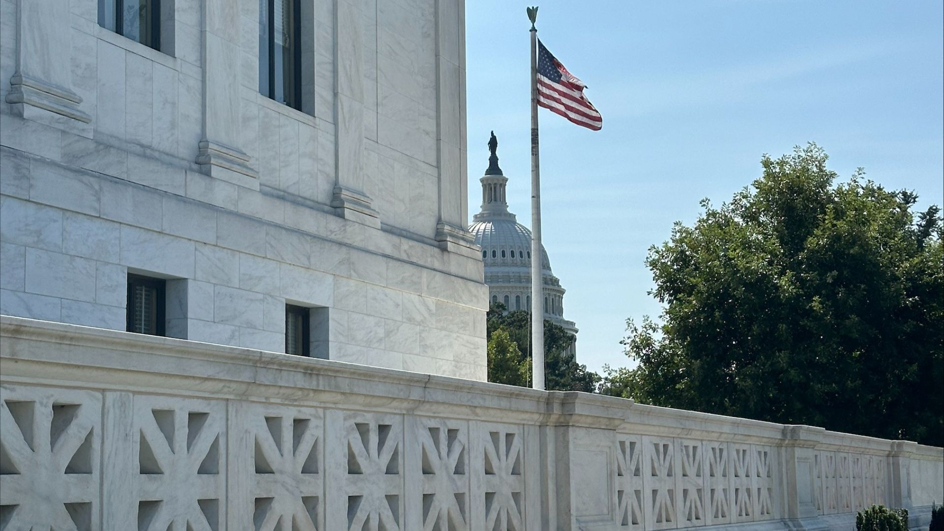 The U.S. Capitol dome emerges from behind the U.S. Supreme Court building and an American flag blows in the breeze